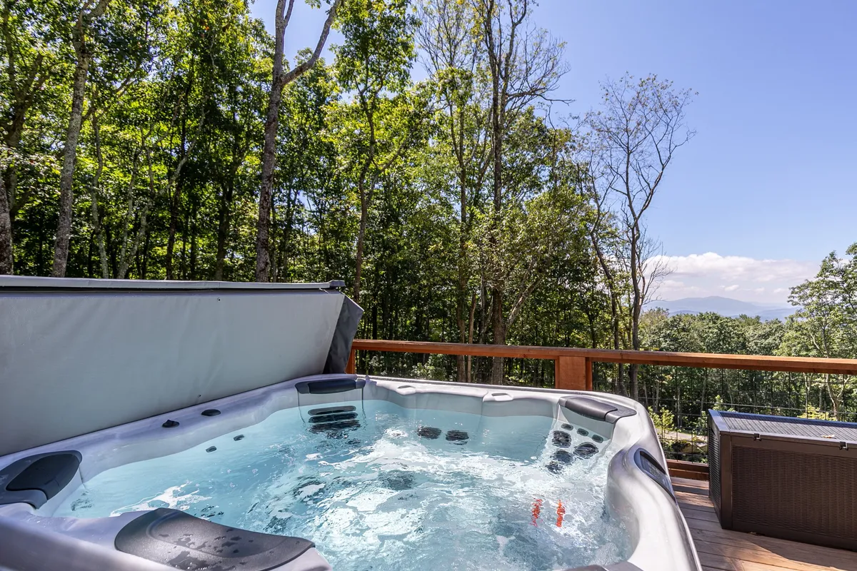 A tranquil hot tub on a deck surrounded by trees provides a peaceful retreat after action-packed days. The view of the forest and the inviting water create an immersive nature experience, perfect for unwinding, reflecting the quiet pleasures of mountain living.