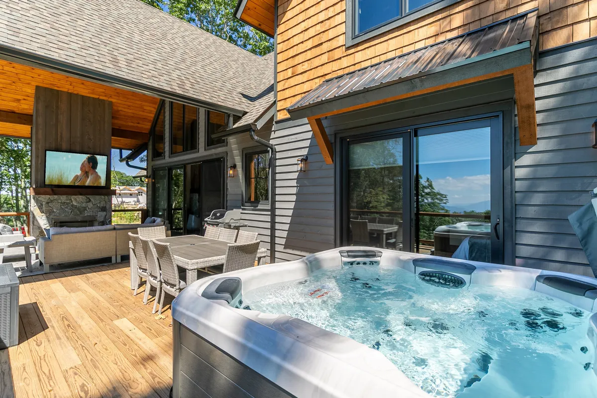 This exterior shot highlights the inviting hot tub, a spacious outdoor seating area, and large windows that connect the indoor and outdoor spaces. The hot tub is set against a backdrop of natural beauty, offering a relaxing spot for both adults and kids after a day of adventure.