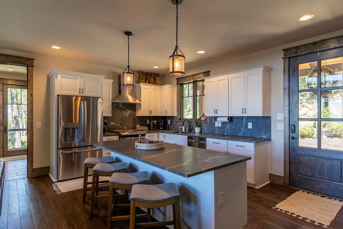 An inviting kitchen with a central island counter, bar stools, stainless steel appliances, and large windows letting in abundant natural light. The space feels both functional and sociable, ideal for culinary adventures and gatherings.