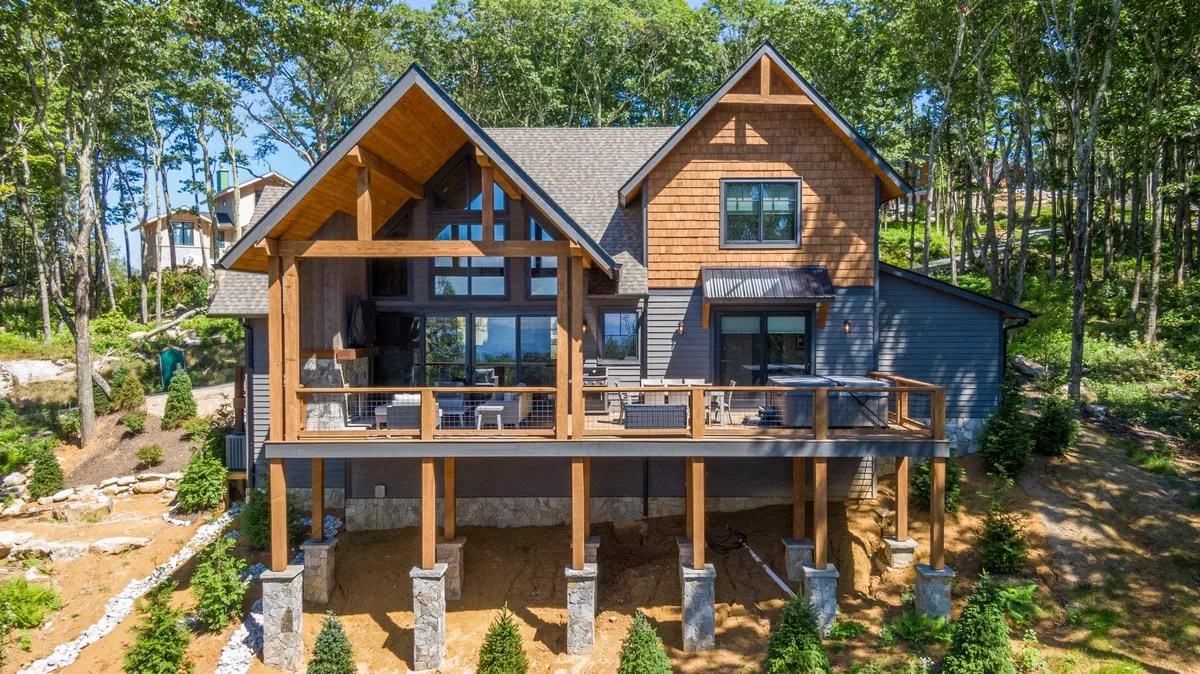 This image captures the home's expansive wooden deck framed by stone pillars and surrounded by lush greenery. The scene shows outdoor dining and relaxation spaces, perfect for groups to gather, share meals, or enjoy nature together. The sunset view hints at evening gatherings and wildlife watching opportunities.
