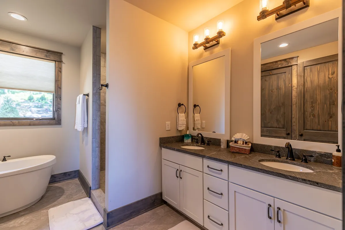 A serene bathroom scene with a freestanding bathtub, double vanity, and a large mirror. Wooden accents and ample morning light create an inviting space for relaxation and self-care.