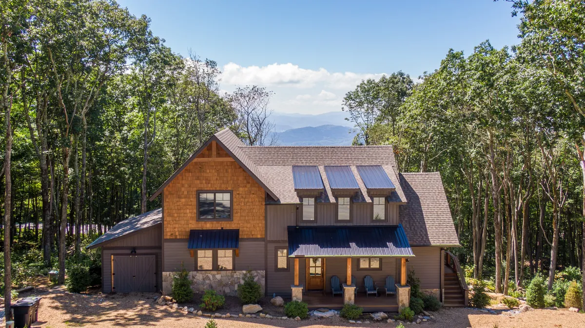 The image captures the front porch of Eagles Nest, featuring comfortable seating, a sloped roof, and natural stone accents. The porch overlooks lush greenery and hints at abundant outdoor space for nature walks and family gatherings.