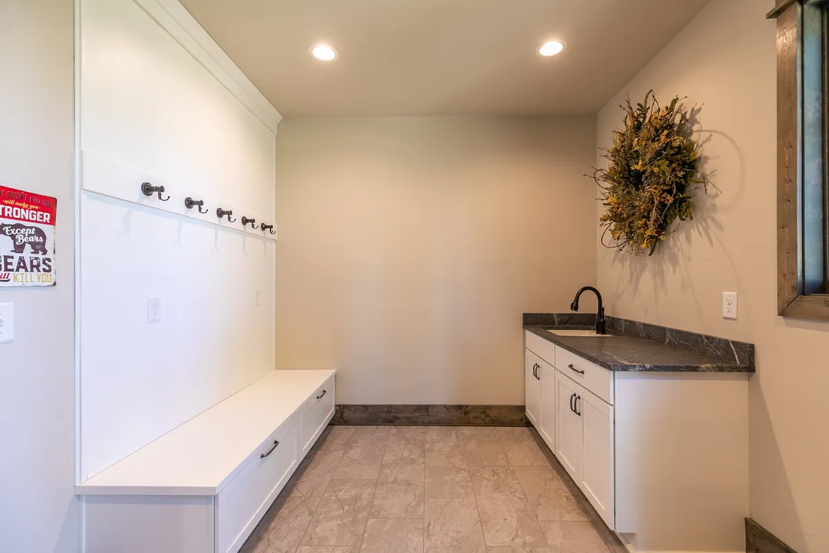A functional mudroom featuring a sturdy bench, hooks for outdoor gear, a sink, and a welcoming wreath. The space is designed for guests to store or clean up after their outdoor adventures.